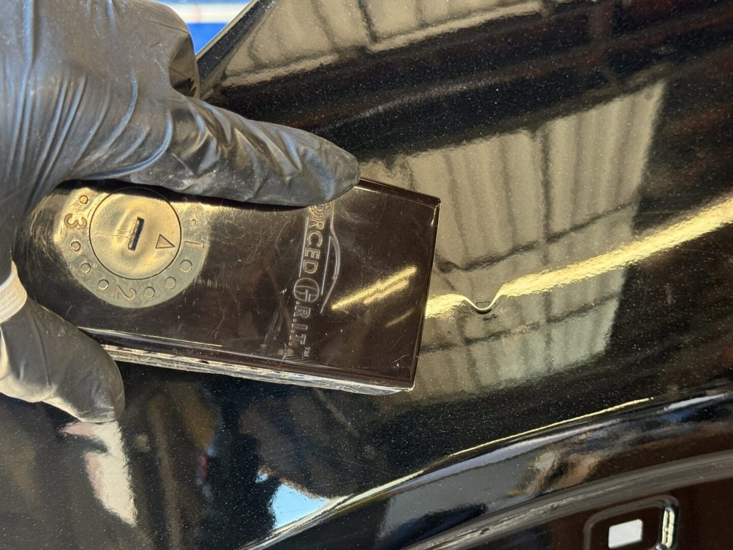 Here's an alt tag for the image: Gloved hand using tool to repair car scratch.