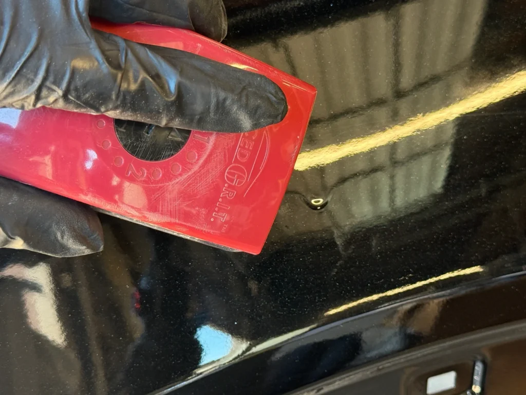 Close-up of a hand using a red tool on a black car surface.