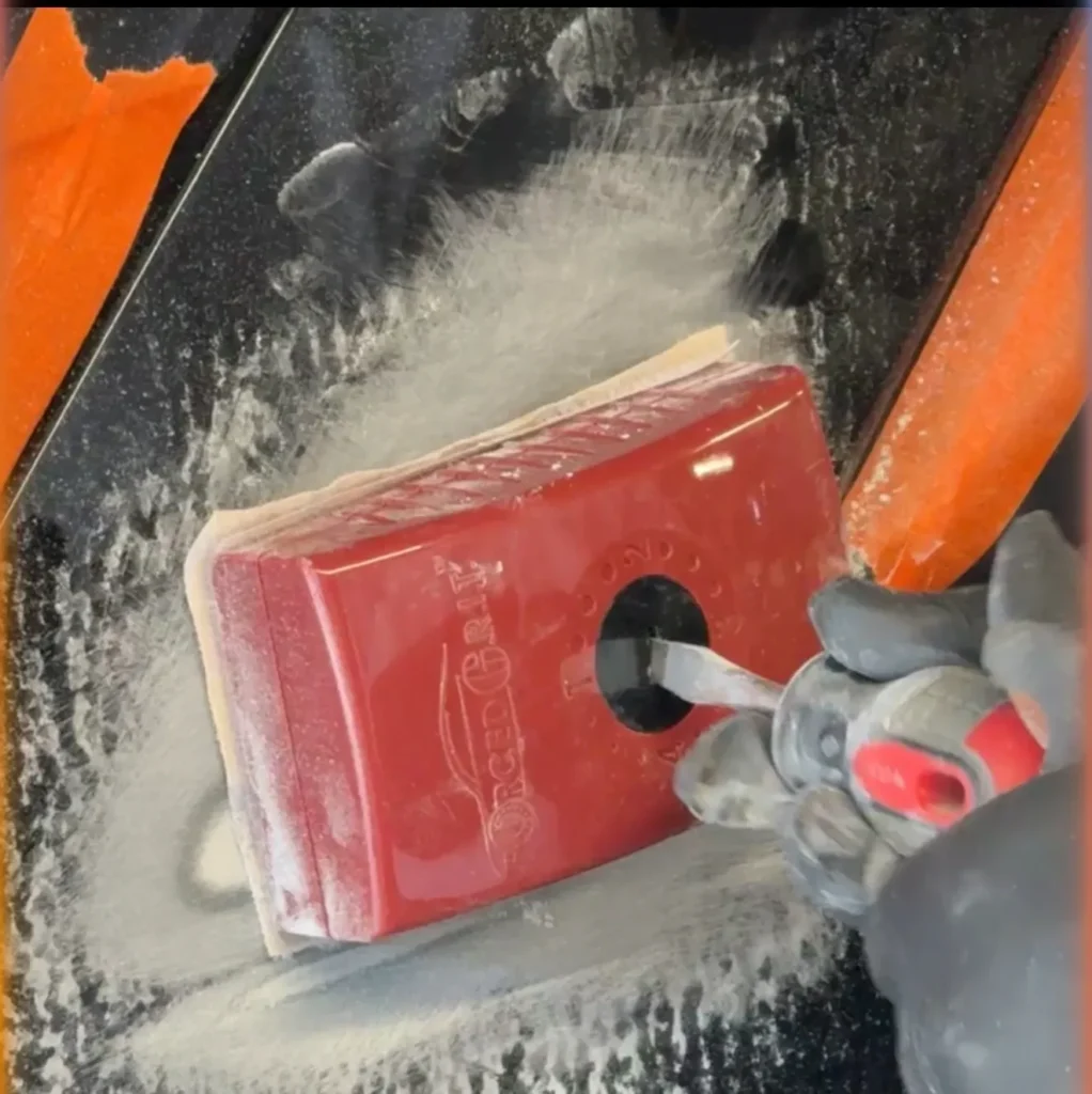 A hand using a tool to polish a red smartphone.