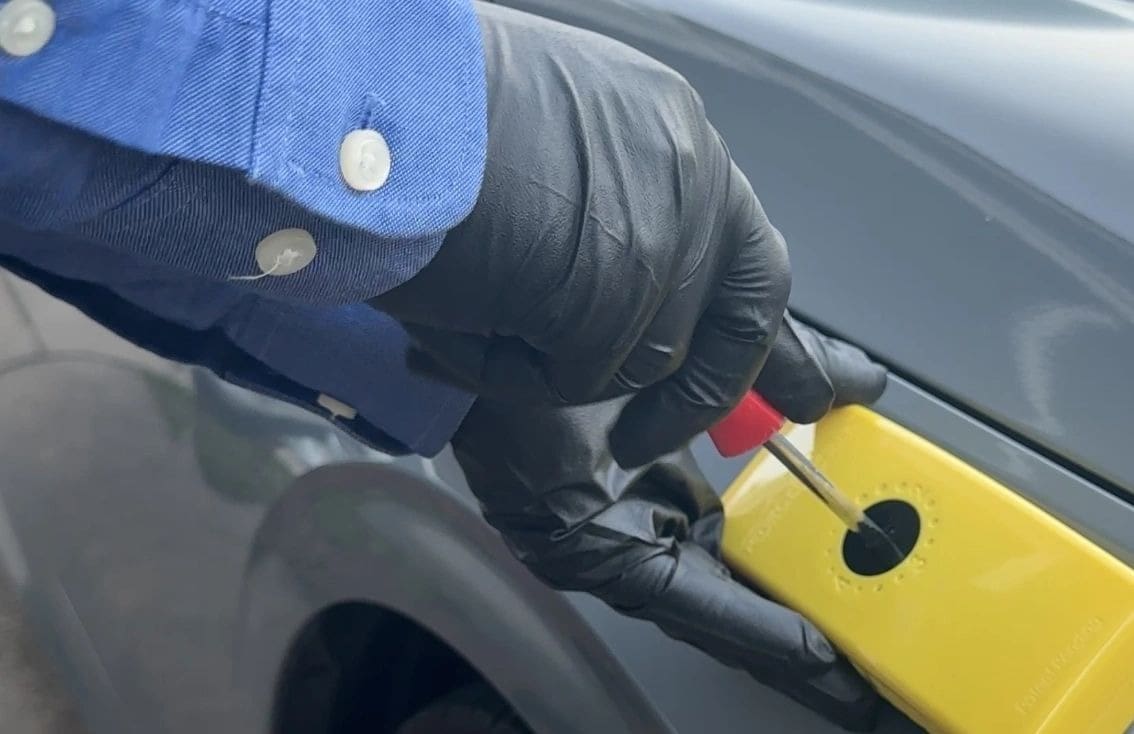Person wearing gloves holds a yellow lockout device on a car door handle.